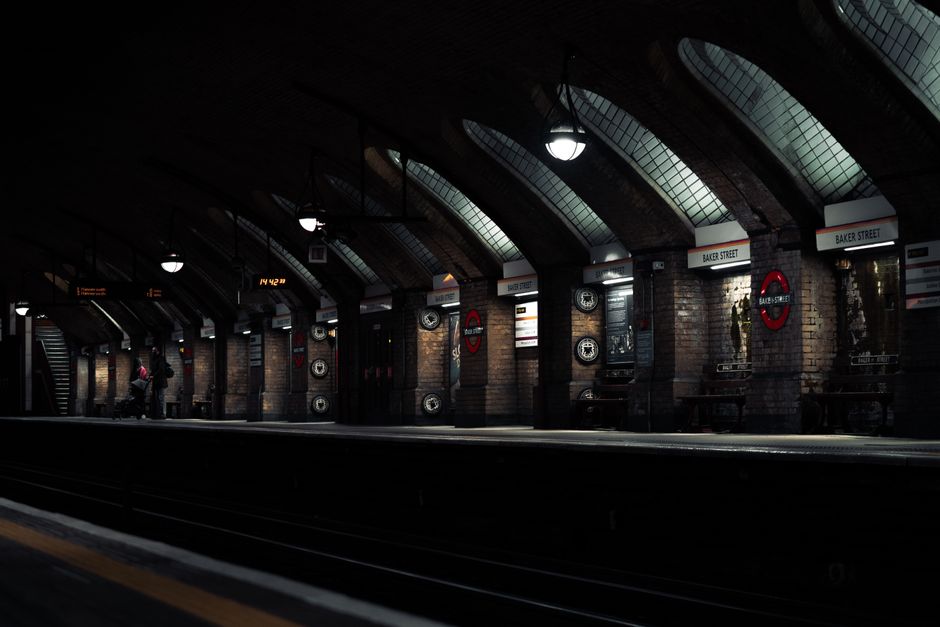 Inside a dimly lit underground train station with arched brick ceilings and large, curved glass skylights allowing some natural light. The platform edge runs along the bottom of the image, with a few