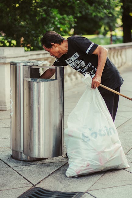 Close-up image of a tightly tied black plastic rubbish bag with visible creases and a glossy finish, placed against a plain, neutral-colored wall. The bag appears full and is located on a surface or i